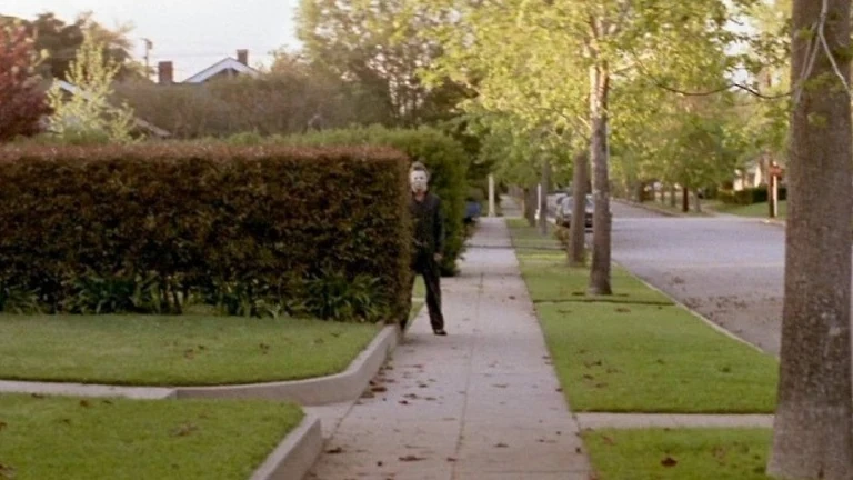 Halloween (1978) — Michael Myers watching from behind a hedge.